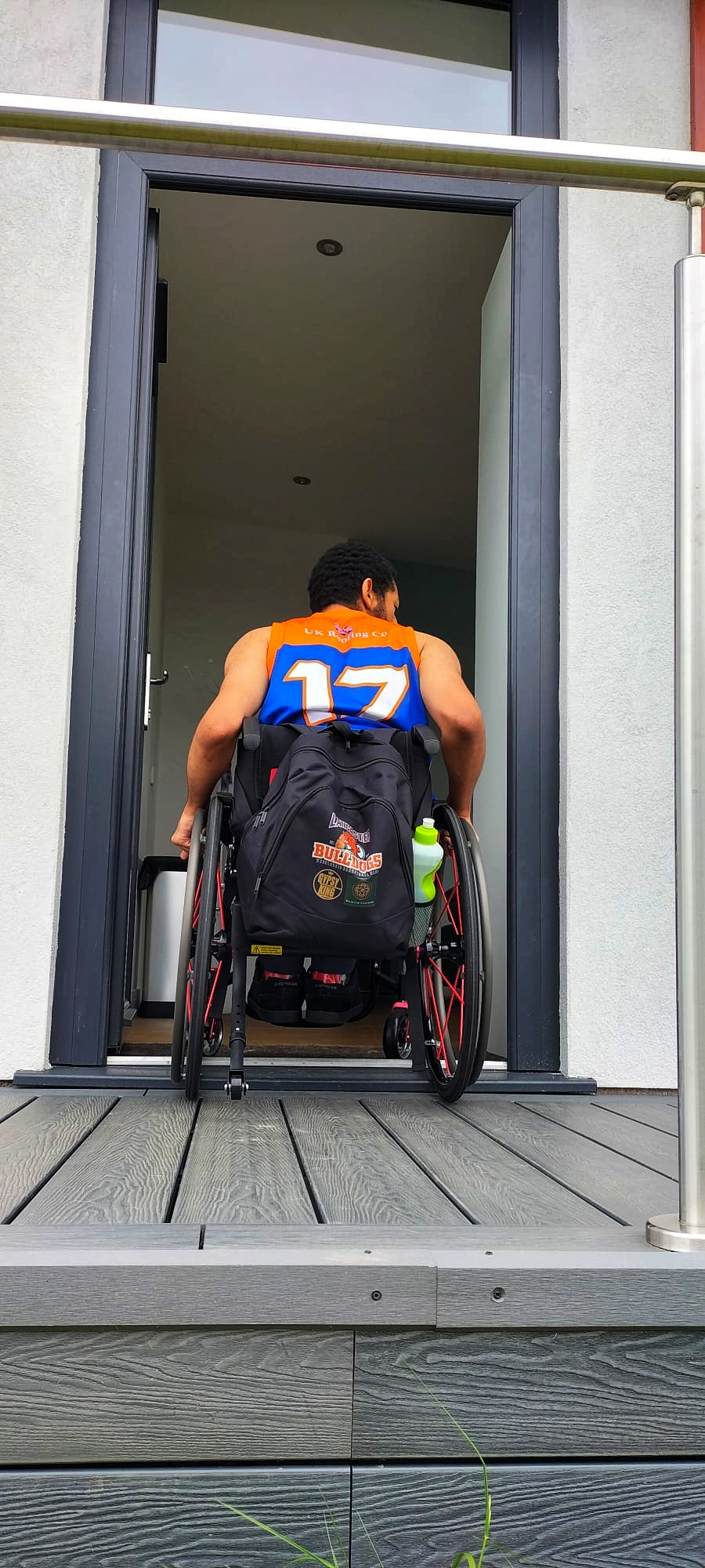 Young man entering the main door in a wheelchair. Brightly coloured top with number 17 on it.