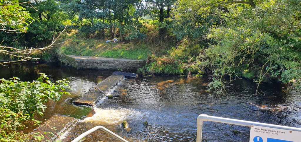 The River Mead in Garstang, Lancashire with a weir surrounded by trees.