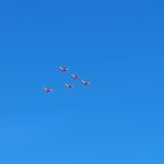 Five Red arrows flying over the field at The Estuary Riverside Chalets in a V formation. Blue cloudless sky