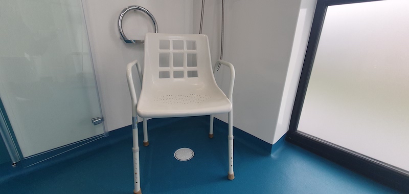 Shower chair in wet room in Bramble. Altro non-slip flooring in teal and white panelled walls. Circular grab rail to shower area with integrated soap dish. Folding shower screen.